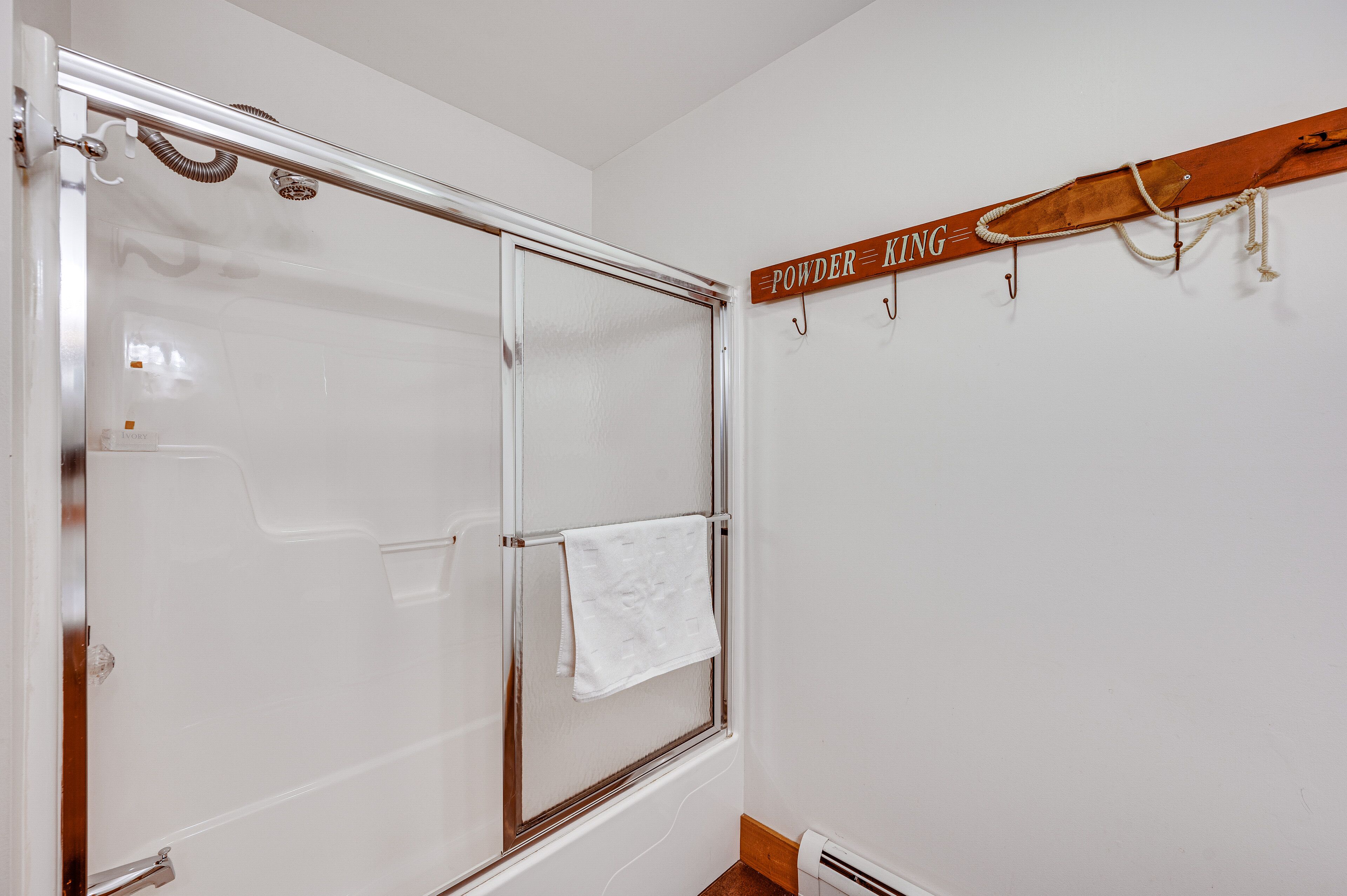 A bathroom with a glass shower enclosure, a towel hanging on the door, and a wooden sign above the shower.