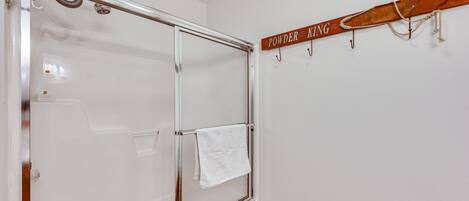 A bathroom with a glass shower enclosure, a towel hanging on the door, and a wooden sign above the shower.