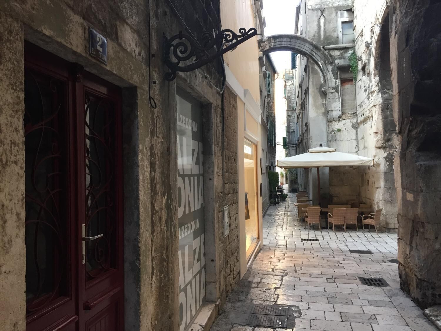 A narrow alleyway with a café featuring outdoor seating and a signboard.