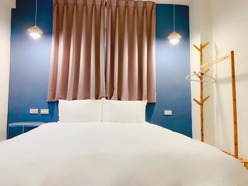 A neatly made bed with a white duvet, a blue wall, and a wooden coat rack with hangers.