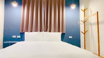 A neatly made bed with a white duvet, a blue wall, and a wooden coat rack with hangers.