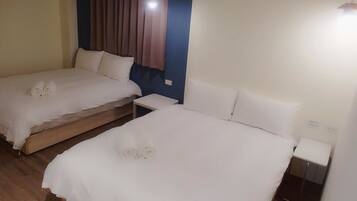 Two single beds with white linens and pillows, a wooden floor, a nightstand with a lamp, and a window with curtains.
