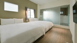 Habitación de hotel con dos camas, un ventanal grande, una puerta corredera de vidrio que da a un área de ducha y un televisor de pantalla plana montado en la pared.
