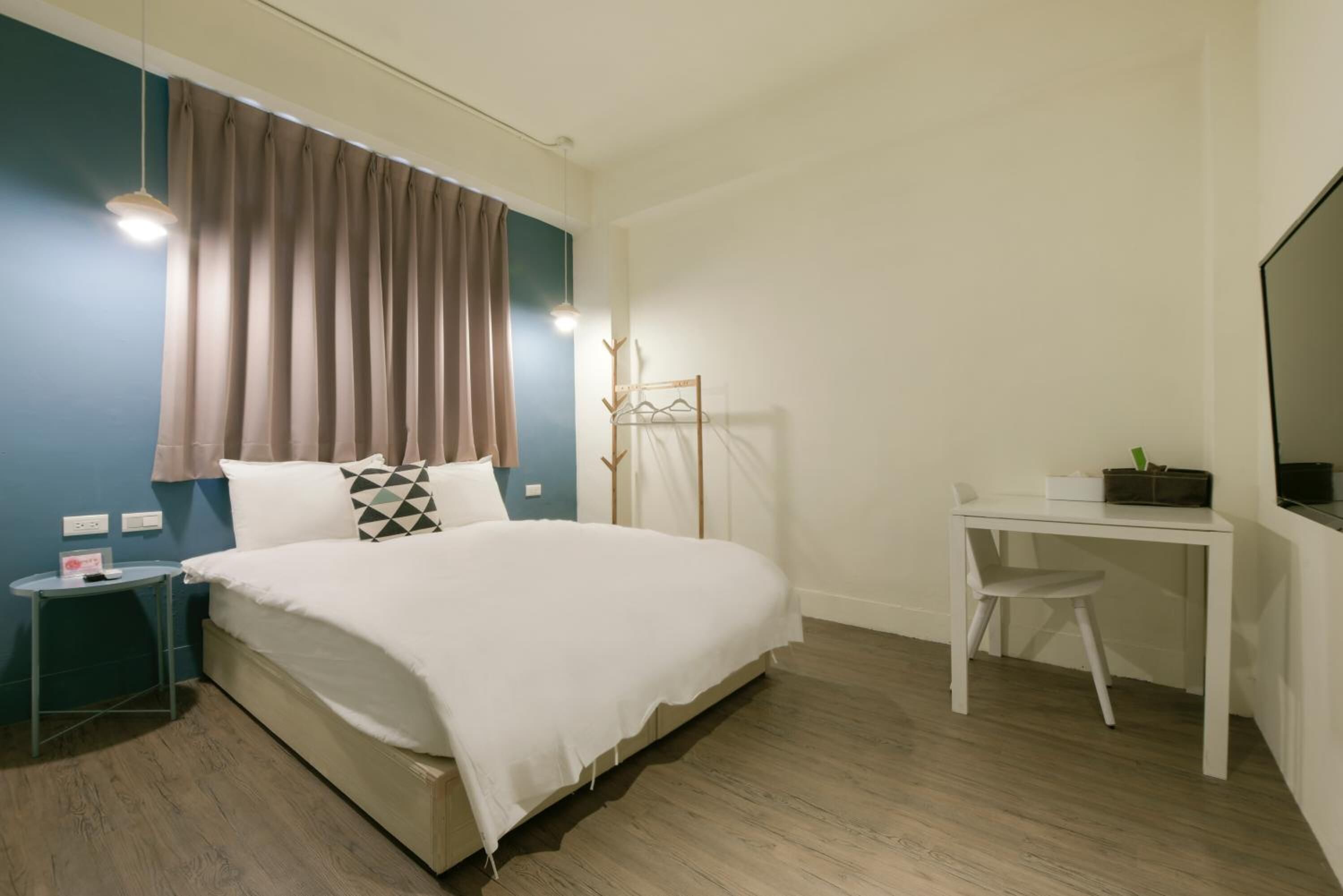 Un dormitorio con cama, mesita de noche, escritorio, silla y televisor en la pared.