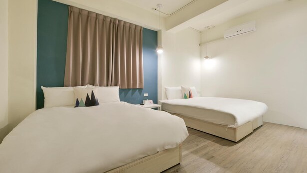 Habitación de hotel con dos camas, una ventana con cortinas, un equipo de aire acondicionado y una mesita de noche con lámpara.