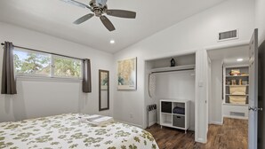 Une chambre à coucher comprenant un lit, un ventilateur de plafond, une fenêtre avec des rideaux, un radiateur, un placard intégré et une porte donnant sur une autre pièce.