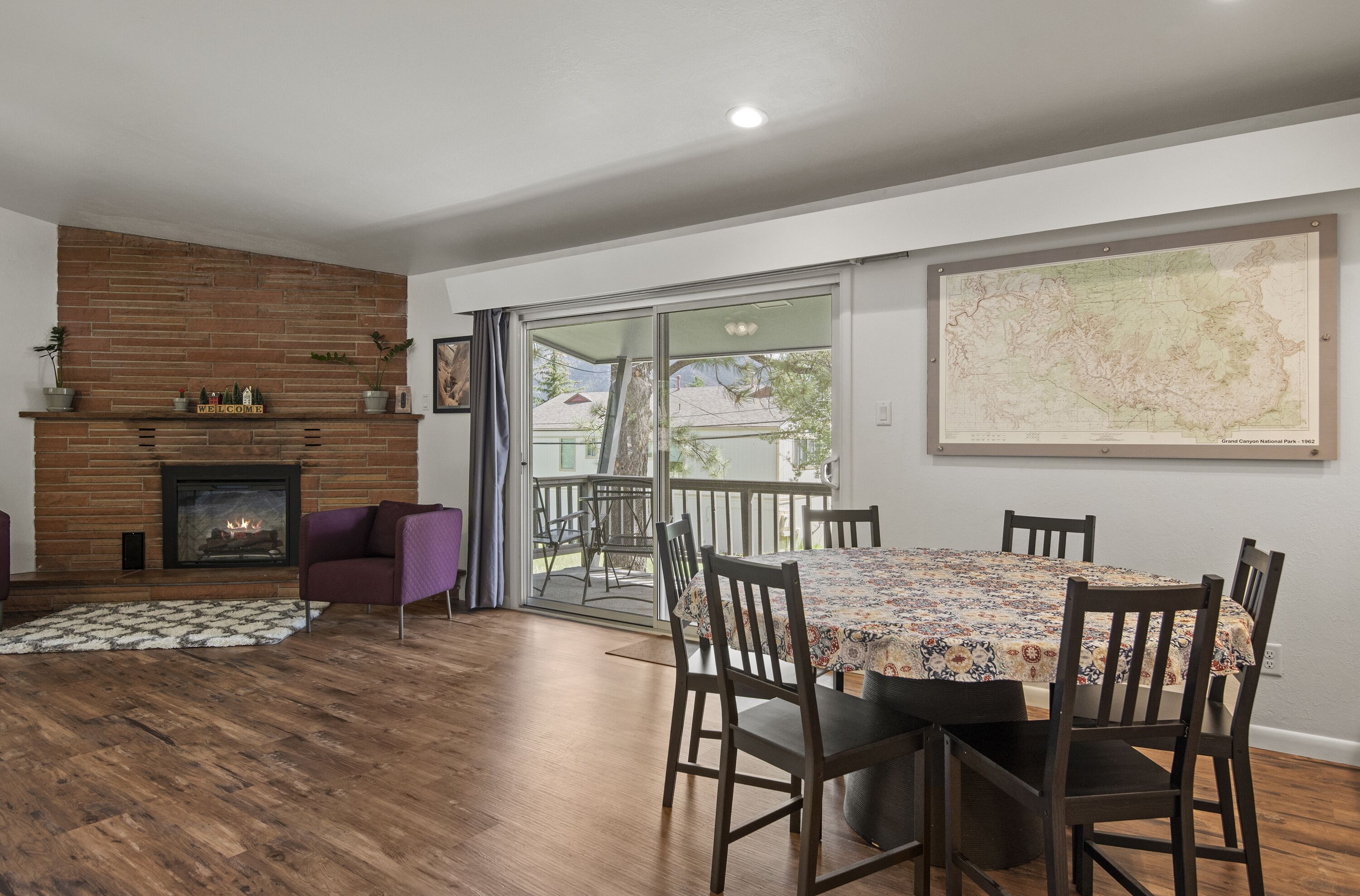 A dining area with a wooden table and chairs, a fireplace, and a large window with a view of the outdoors.