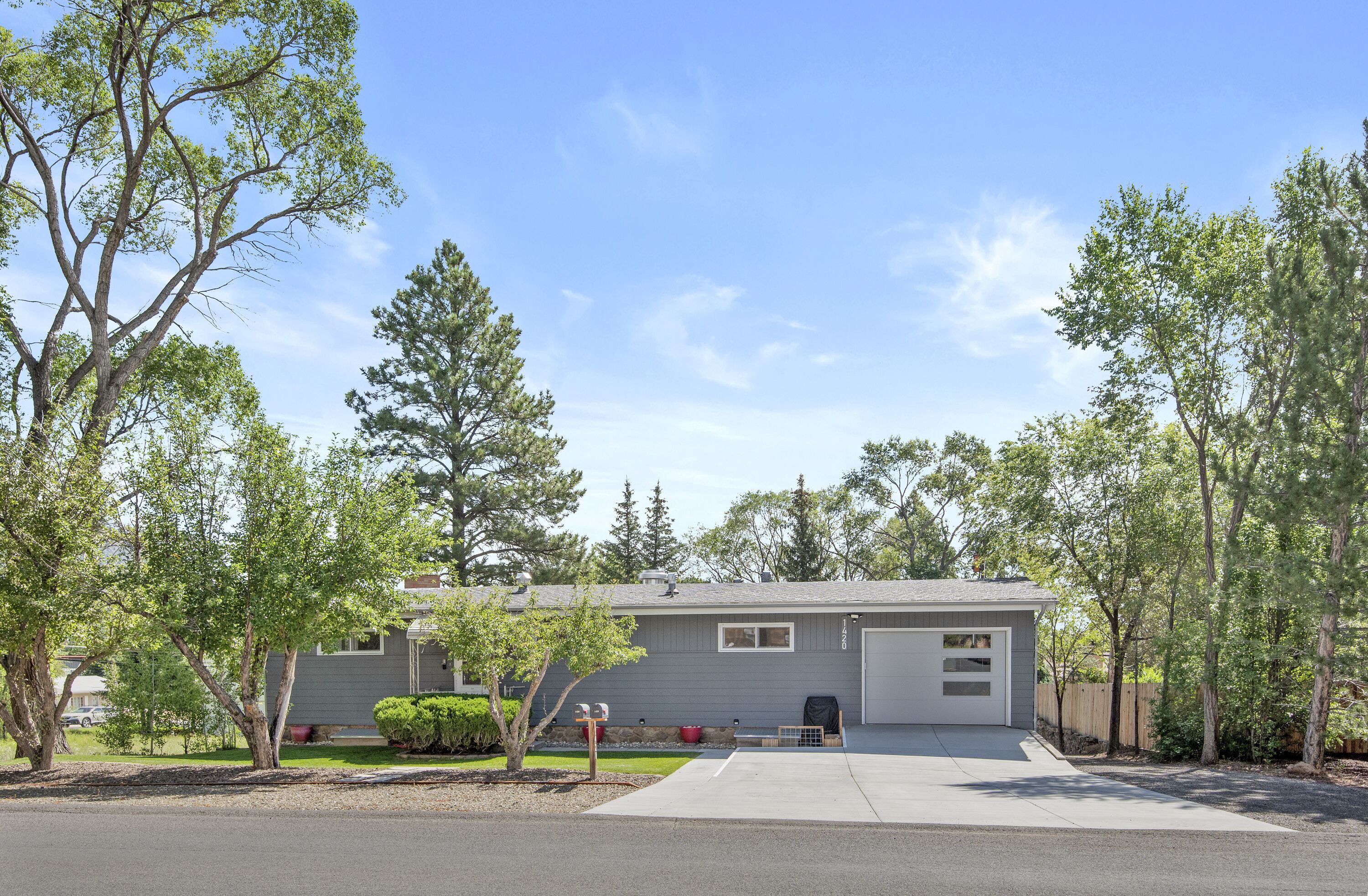 A single-story house with a garage, surrounded by trees and a clear sky.