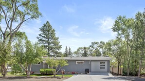 Une maison de plain-pied avec un garage, entourée d’arbres et sous un ciel dégagé.