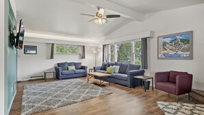 Un salon spacieux doté d’un ventilateur de plafond, de deux canapés, d’une table basse et d’une grande fenêtre laissant entrer la lumière naturelle.