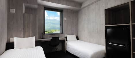 A hotel room with two single beds, a desk, a chair, a window with a view, and a black refrigerator.
