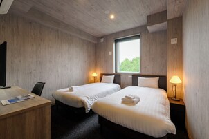 Une chambre d’hôtel avec deux lits, un bureau et une fenêtre donnant sur des arbres.