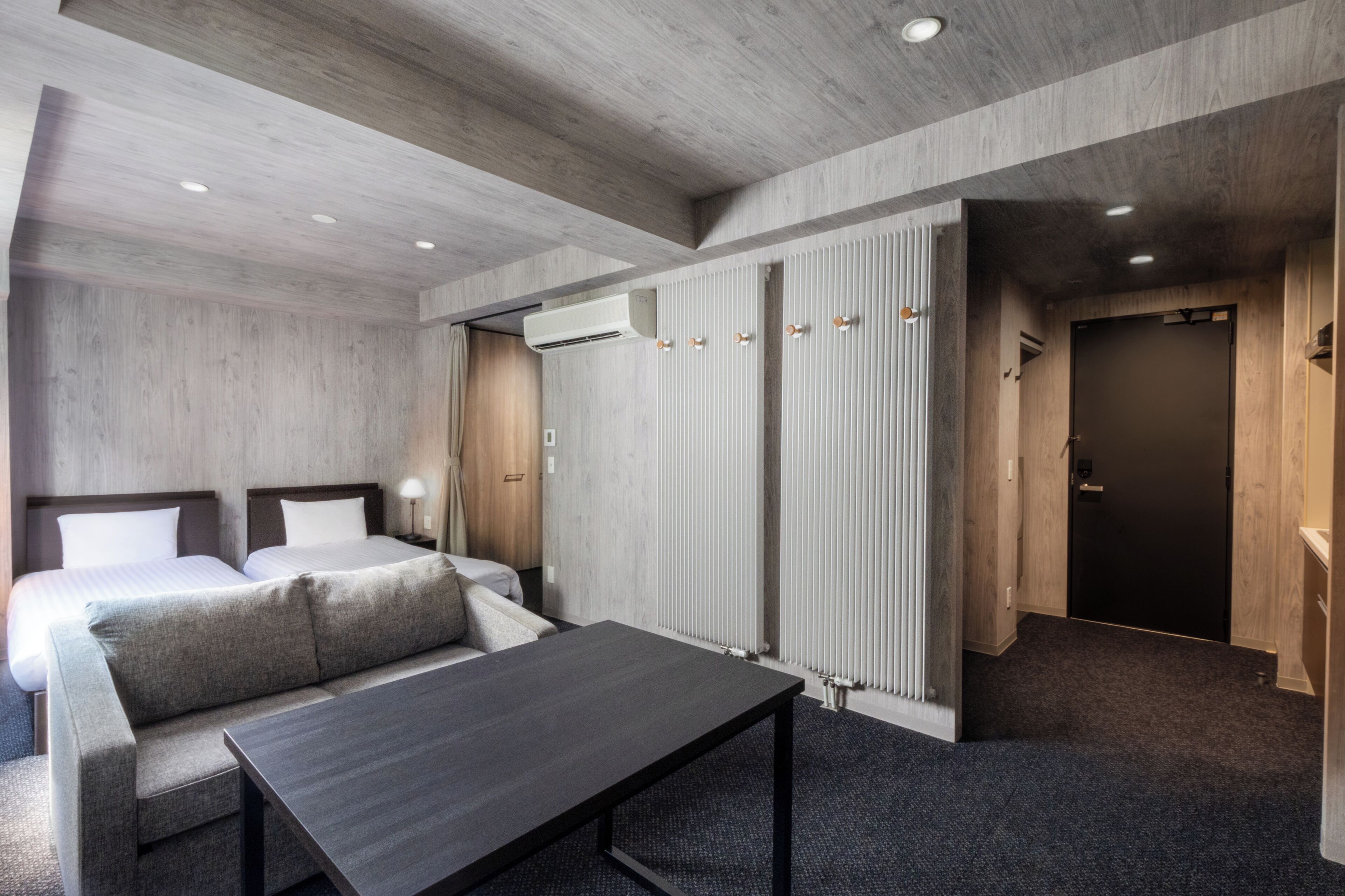 A hotel room with a bed, a desk, a radiator, and a door.