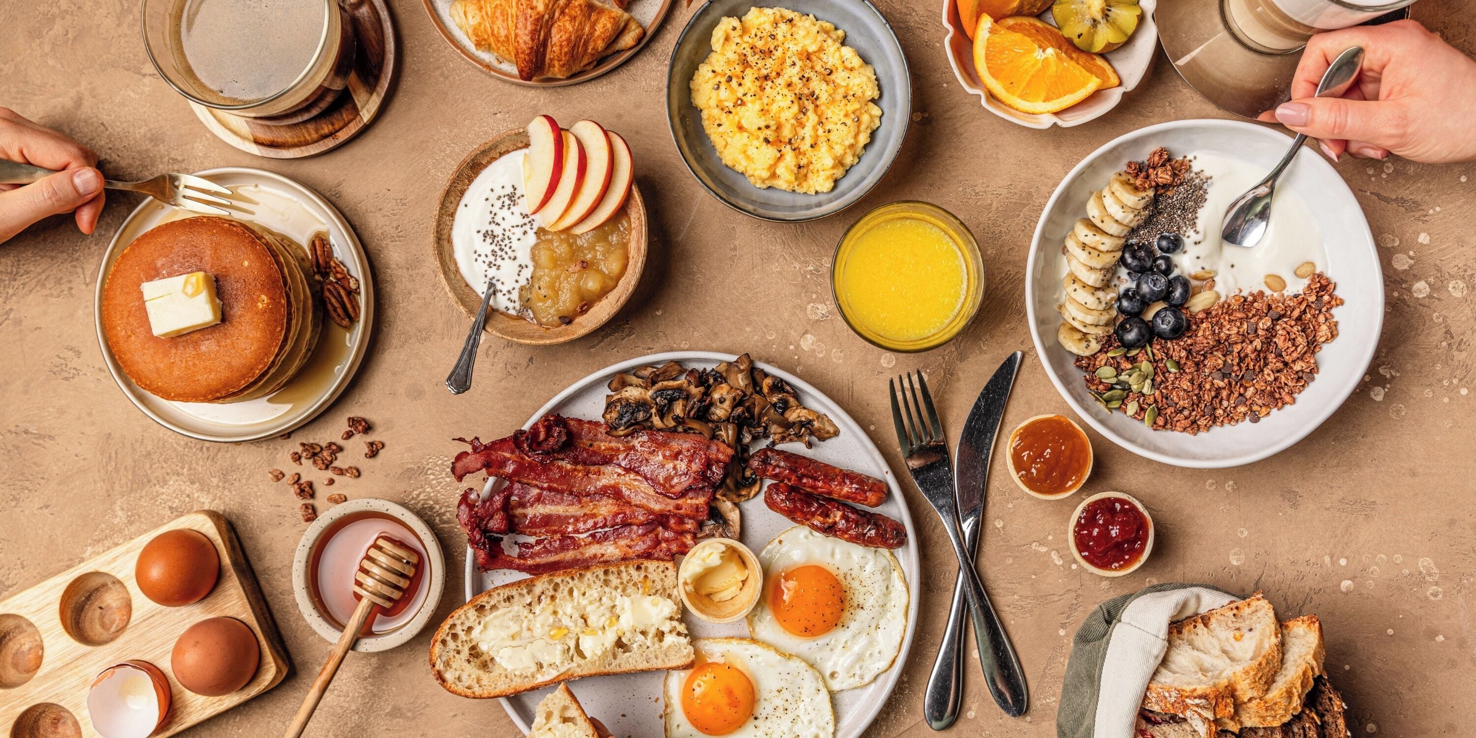 Un desayuno abundante con panqueques, huevos, tocino y diversas frutas y pasteles.