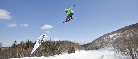 A snowboarder in mid-air performing a jump with a clear blue sky and a snowy landscape in the background.