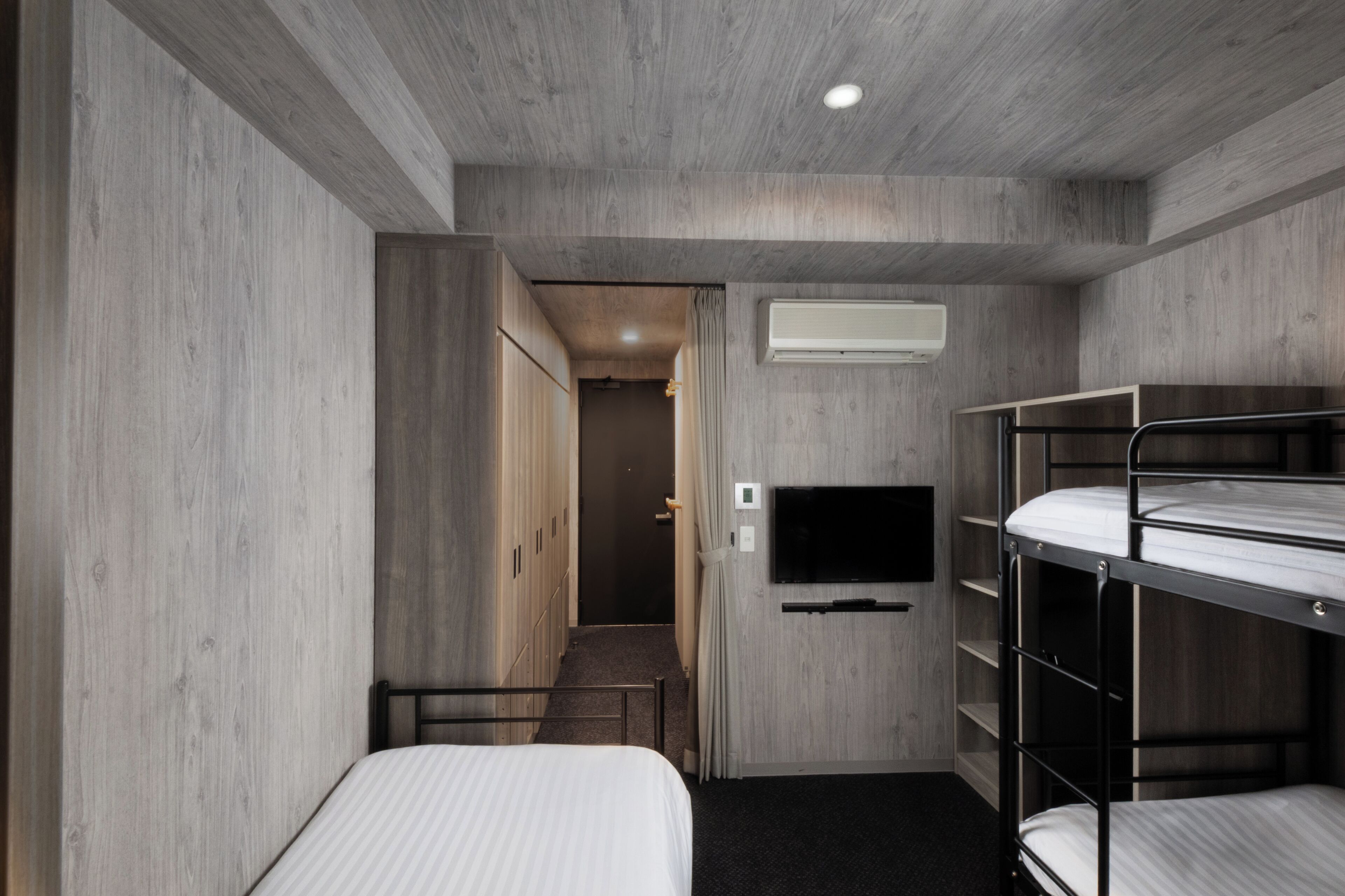 A compact room with bunk beds, a flat-screen TV, an air conditioning unit, and a door leading to a hallway.