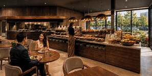 Un restaurante moderno con zona de comedor central, cocina al fondo y vistas a la calle a través de amplios ventanales.