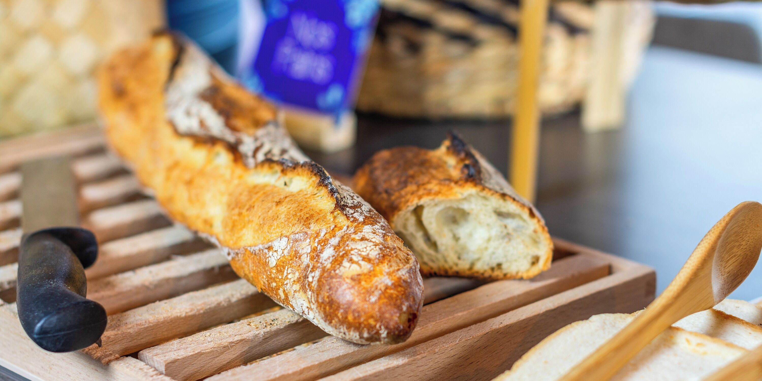 Ein Brot auf einem Holzschneidebrett, zusammen mit einem Messer und einem Holzlöffel.