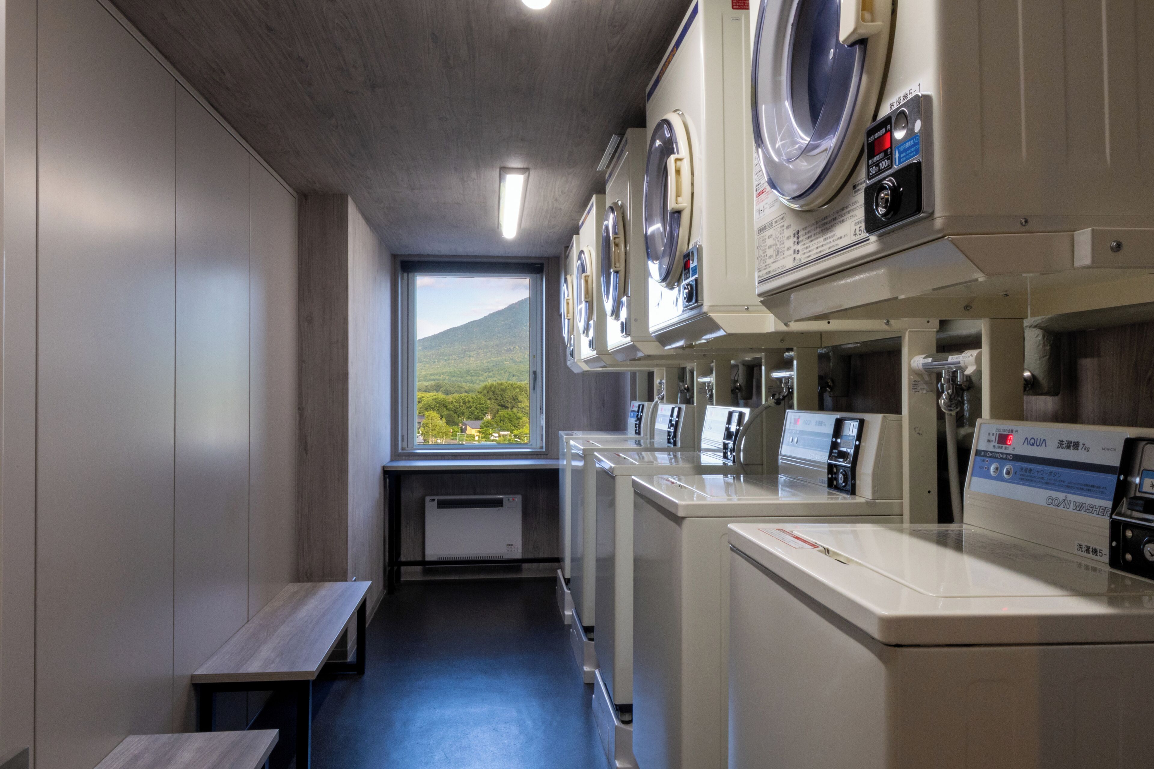 A laundry room with multiple washing machines and dryers, a bench, and a window with a view of a mountain.