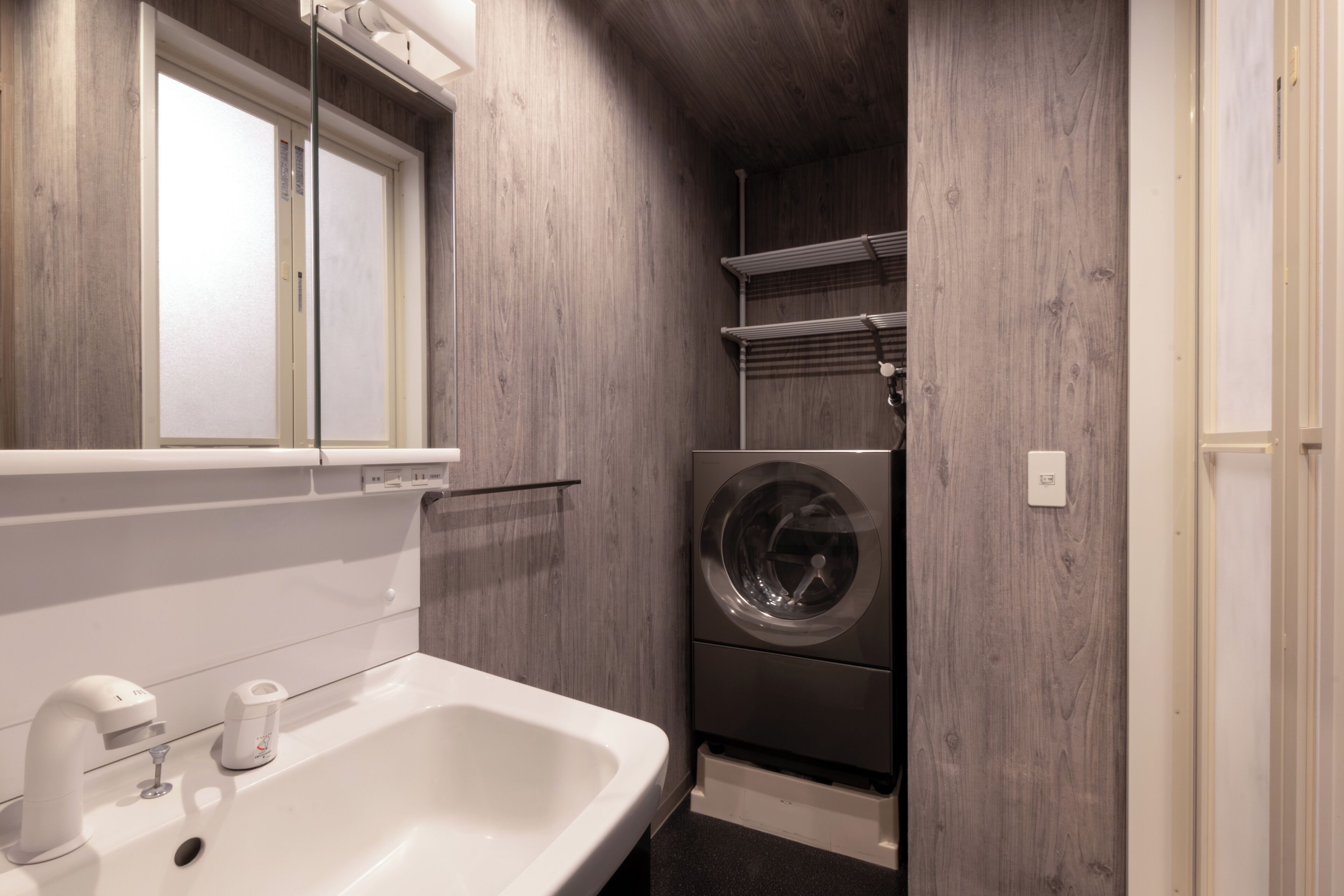 A compact bathroom with a sink, mirror, and a built-in washing machine.