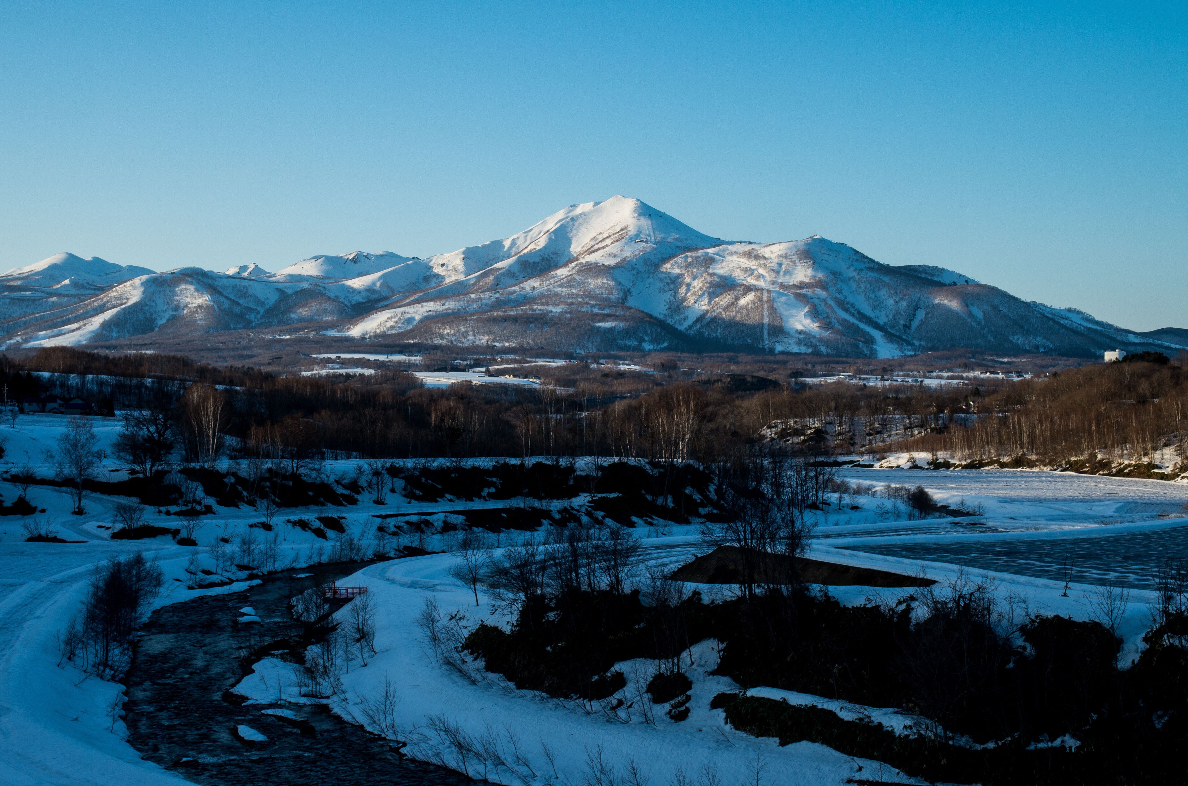 A snow-covered mountain landscape with a river and sparse vegetation.