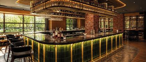 A bar area with a curved counter, multiple shelves of bottles, and a view of greenery outside.