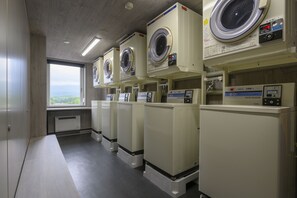 A laundry facility with multiple washing machines and dryers, a window with a view, and a tiled floor. - Mercure Niseko Resort (Formerly known as Midtown Niseko) (Kutchan)