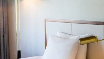 A neatly made bed with white linens and a gold bedside lamp.