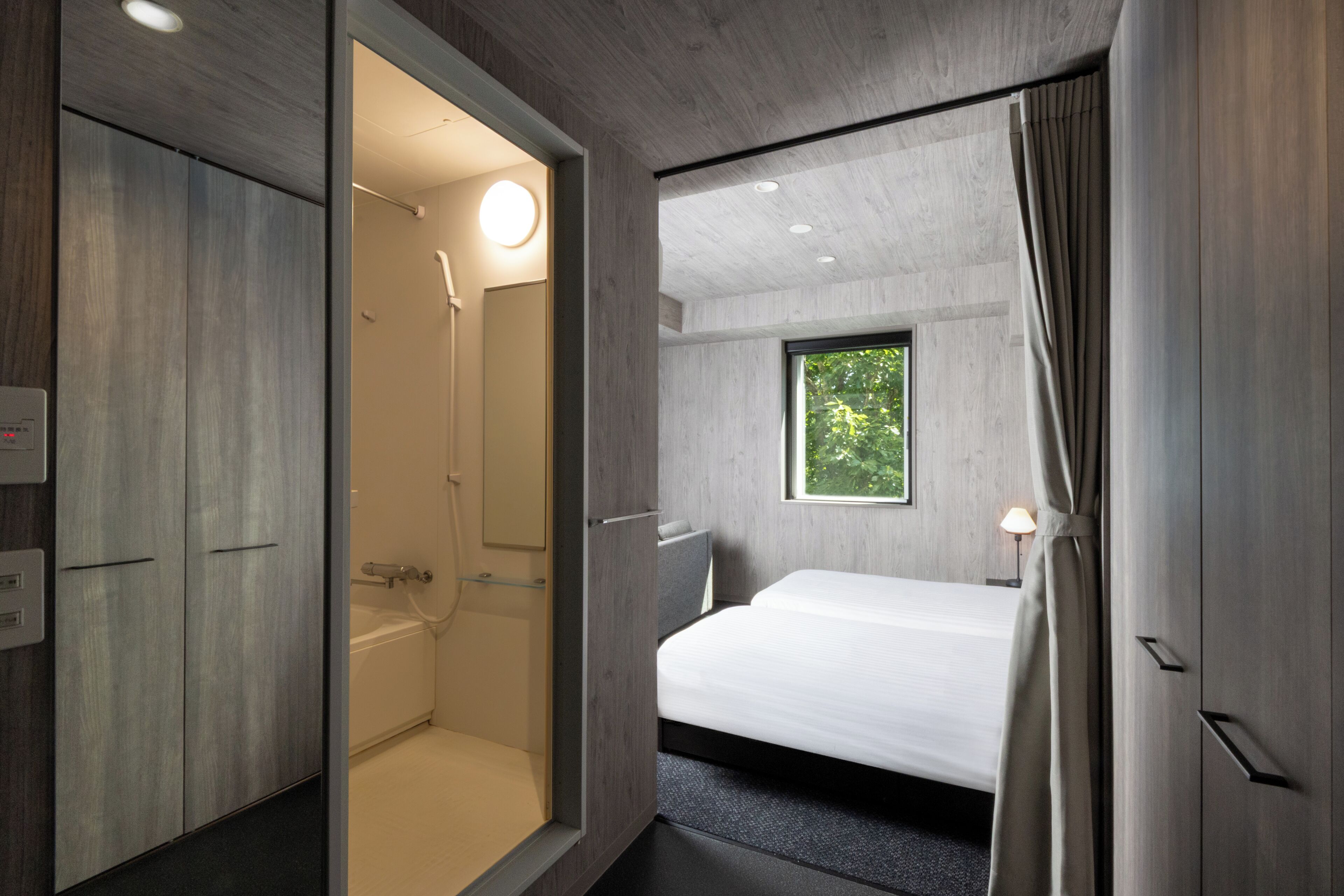 Ein modernes Hotelzimmer mit Dusche, einem Bett und einem Fenster mit Blick auf Grünflächen.