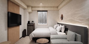 A modern bedroom with a bed, a sofa, a TV, and a window with a view of trees. - Mercure Niseko Resort (Formerly known as Midtown Niseko) (Kutchan)