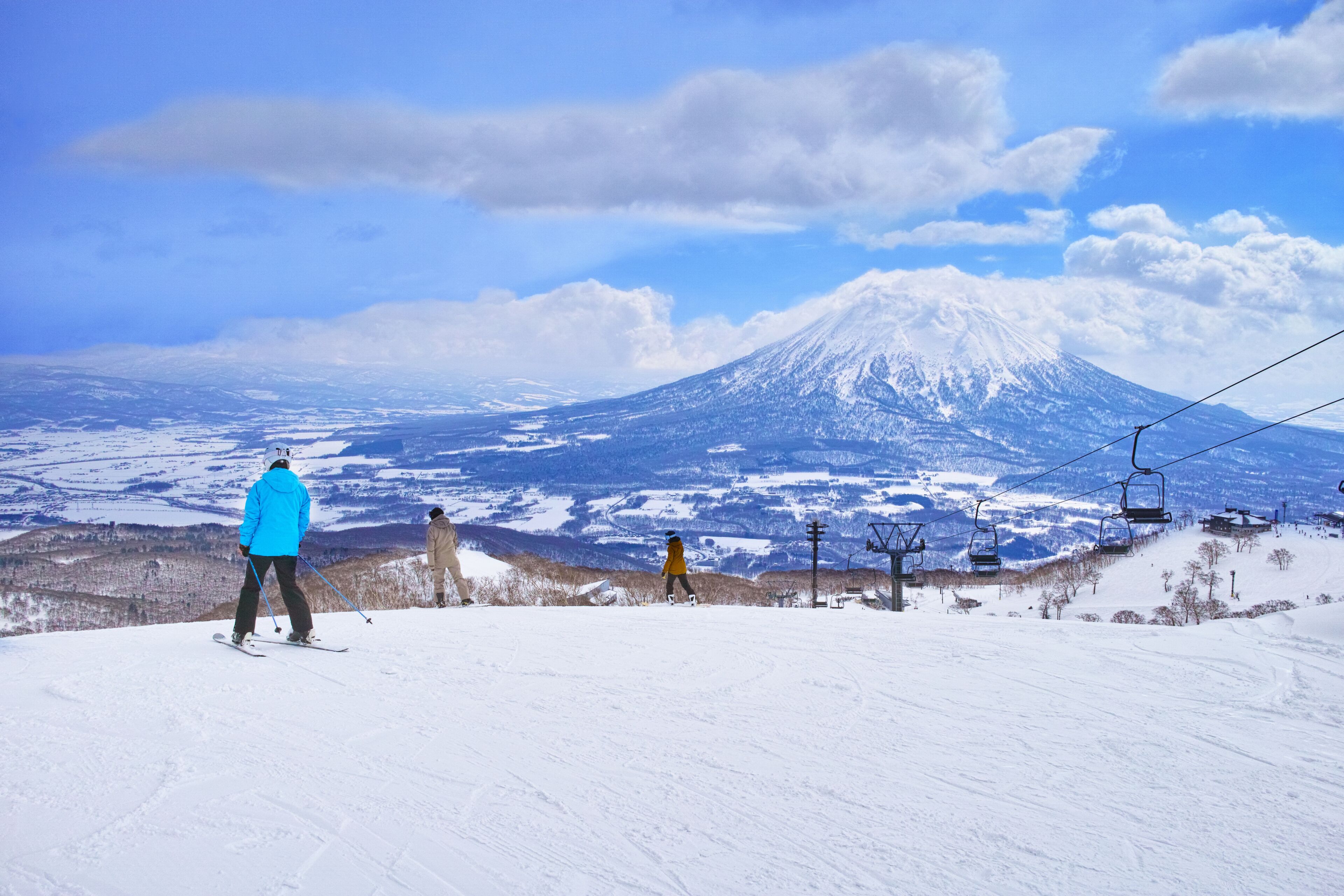 A ski slope with a mountain in the background, ski lifts, and a clear sky.