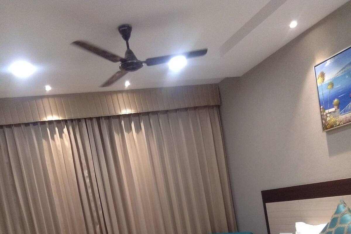 Een hotelkamer met een bed, gordijnen, een plafondventilator en een schilderij aan de muur.