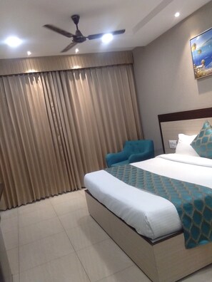 A hotel room with a bed, curtains, a ceiling fan, and a painting on the wall. - Aagaaz for Luxury Stay and Celebration (Ludhiana)