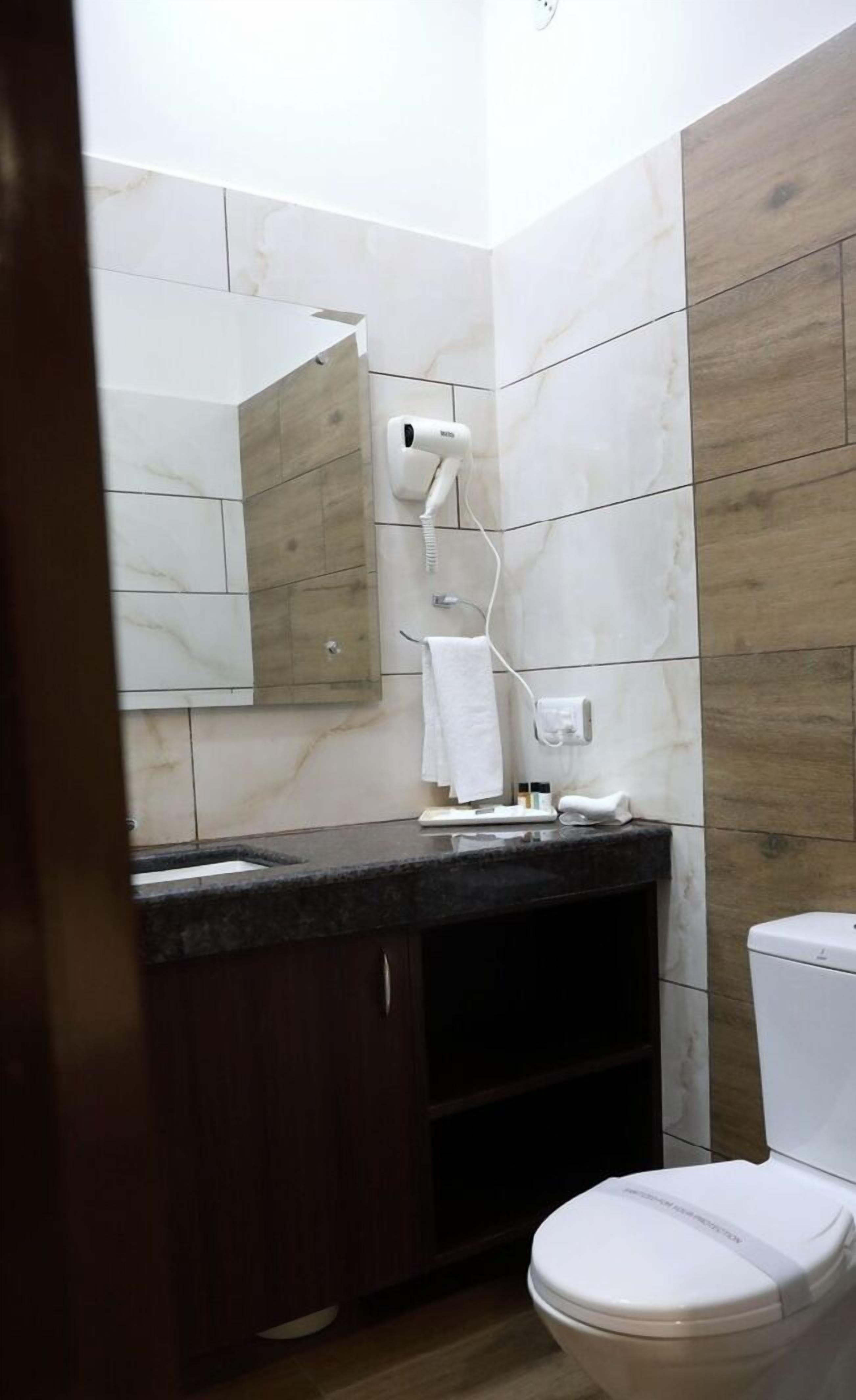 A bathroom with a white toilet, a wooden vanity with a mirror, and a hairdryer mounted on the wall.