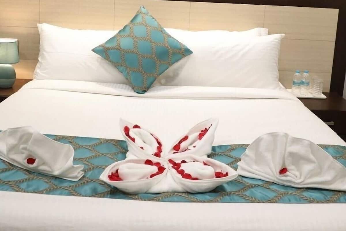 Een hotelkamer met een bed, kussens, een schilderij van de Eiffeltoren en een netjes opgevouwen handdoek.