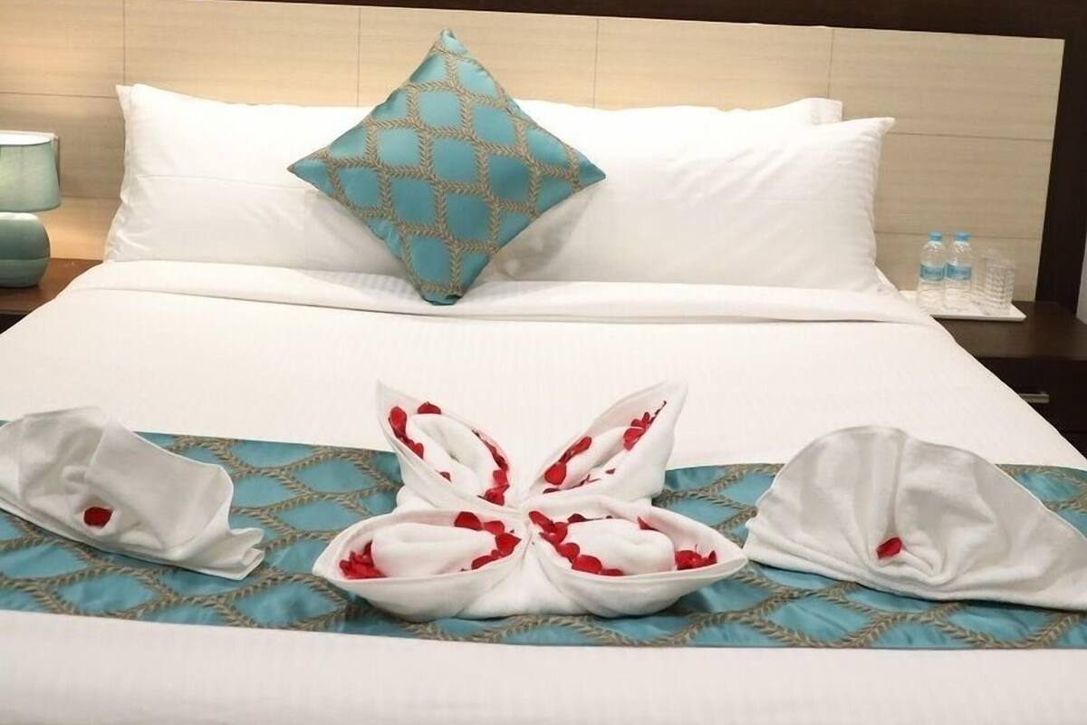 Een hotelkamer met een bed, kussens, een stadsgezicht op een schilderij en een decoratieve handdoekopstelling.