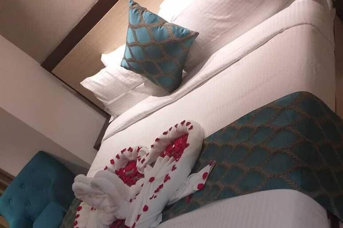 Een hotelkamer met een groot bed, een blauwe fauteuil en een decoratieve handdoek met rode bloemen.