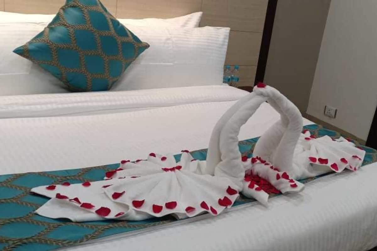 Een hotelkamer met een bed, voorzien van een witte spreidek en een blauwe bedrok met patroon. Op het bed staan twee decoratieve zwanen, gemaakt van witte stof en rode rozenblaadjes.