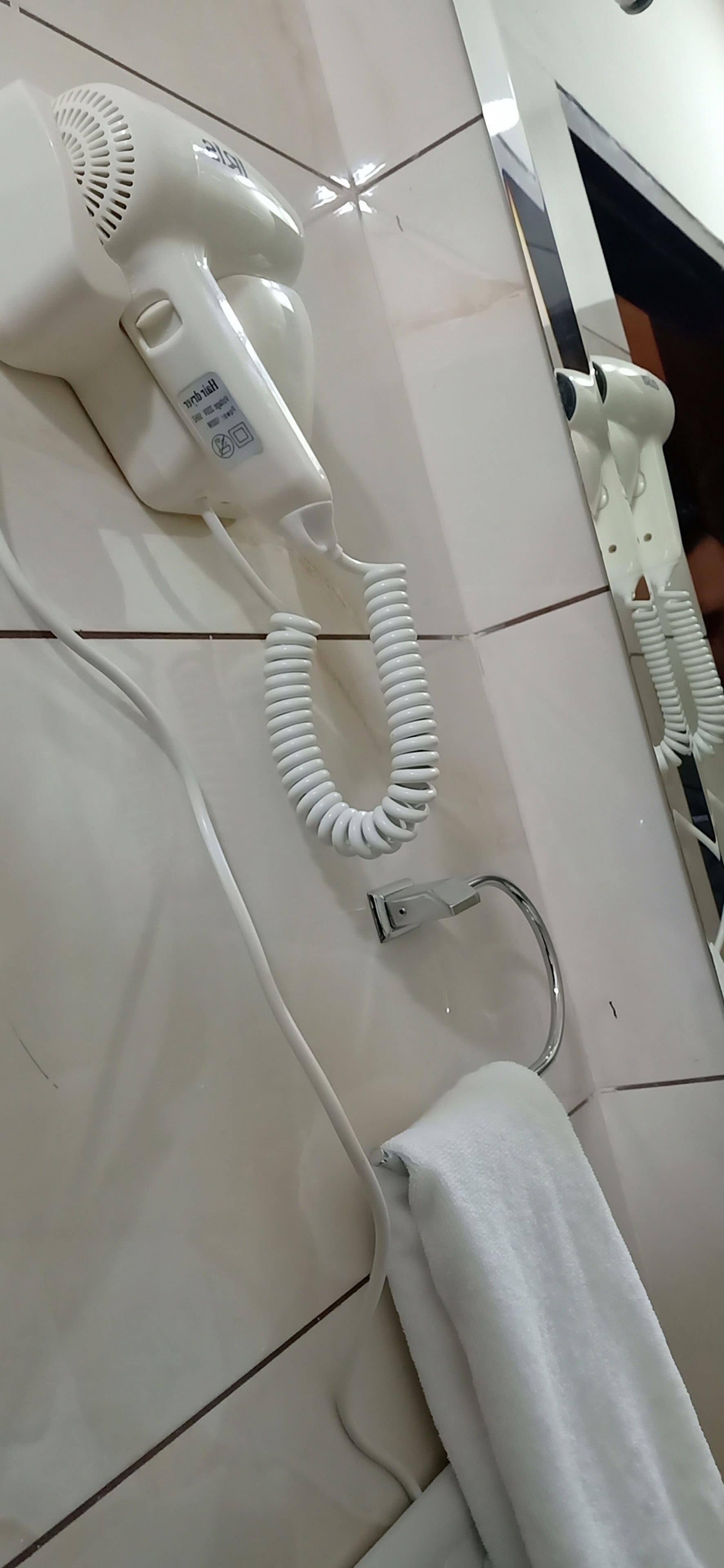 Un sèche-cheveux et un porte-serviettes fixés à un mur carrelé.