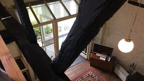 Una habitación con techos altos, un gran ventanal, una escalera de madera, un tapete rojo con motivos, un televisor y una lámpara colgante.