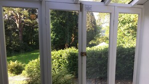Un invernadero con puerta de cristal que ofrece vistas a un jardín exuberante, con diversas plantas y un sendero de grava.