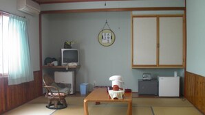 Una habitación japonesa tradicional con suelo de tatami, televisión, refrigerador y un armario de madera.