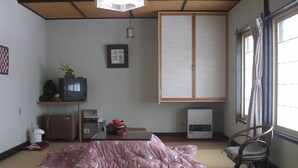 Una habitación japonesa tradicional con suelo de tatami, futón, televisión, armario y puerta corredera.