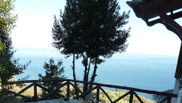 Un área de estar al aire libre con una mesa, sillas y un banco acolchado, con vista al mar.