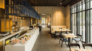 Een modern restaurant met een lange toonbank waarop eten en drinken staan uitgestald, een zithoek met tafels en stoelen, en grote ramen met uitzicht.