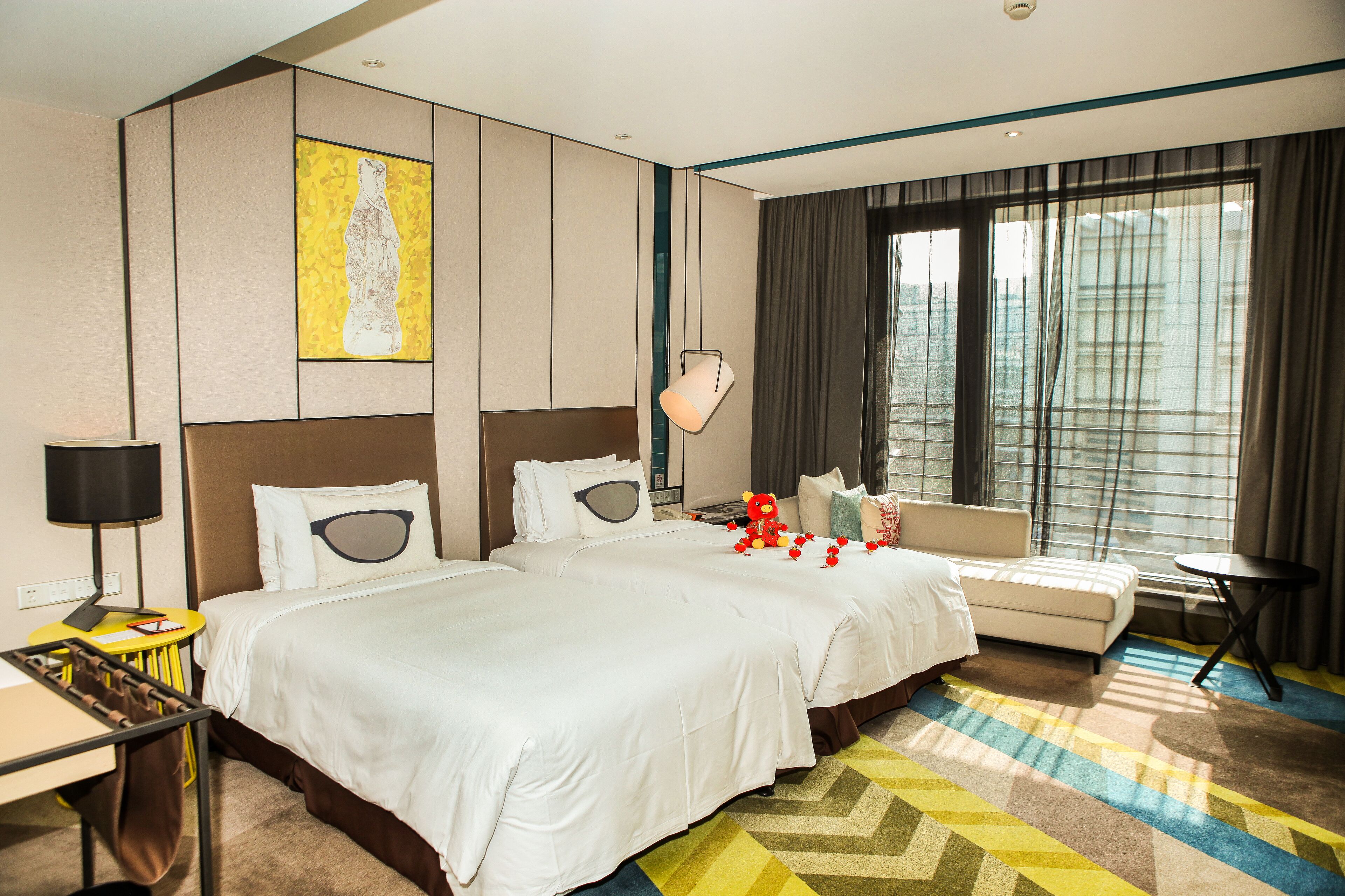 A hotel room with a large bed, a sofa, a small table, and a window with curtains.