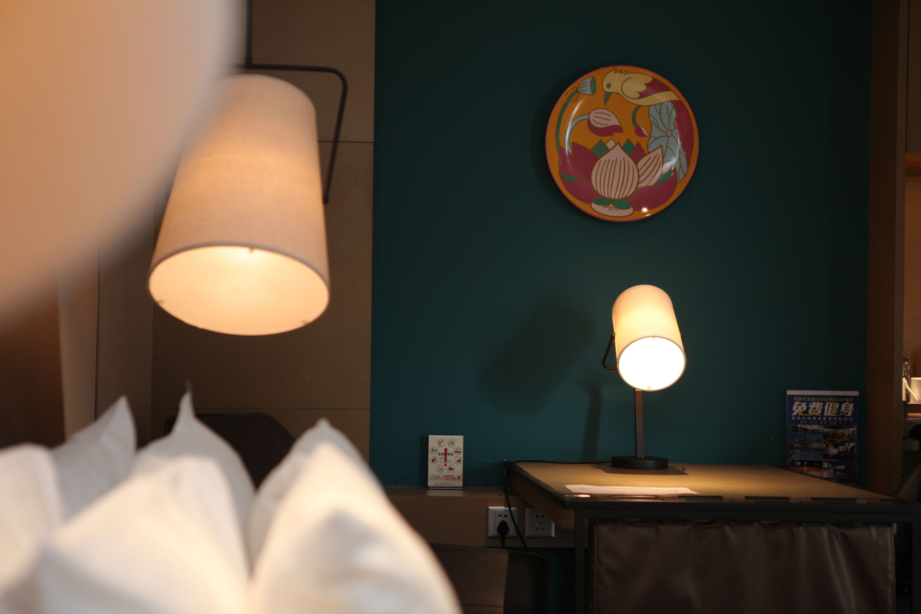 Une chambre d’hôtel avec un lit, une table avec une lampe, une horloge murale et une assiette décorative.
