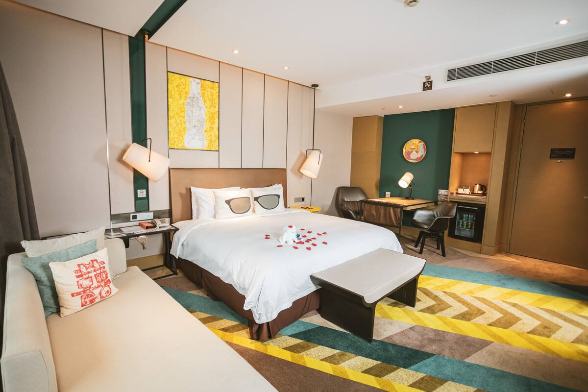 A hotel room with a bed, a desk, a chair, a sofa, and a small table.