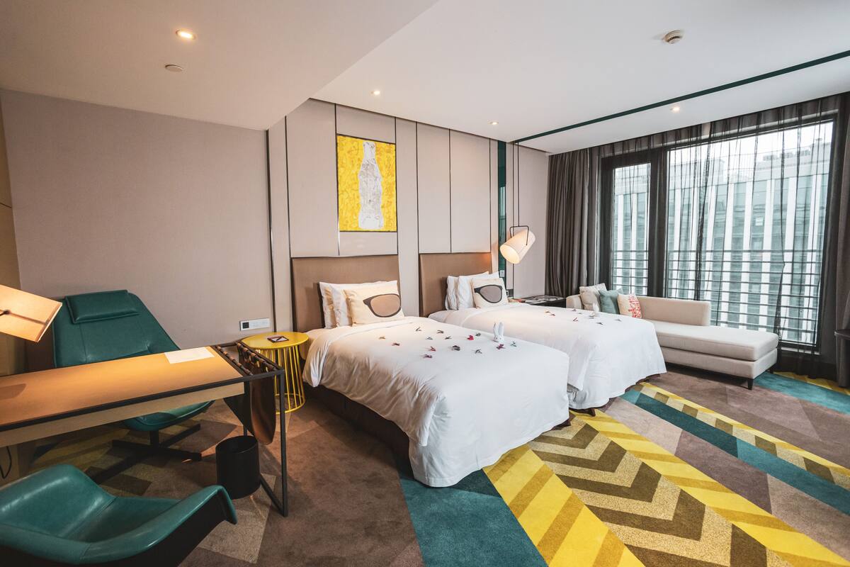 A hotel room with two beds, a sofa, a desk, and a chair.