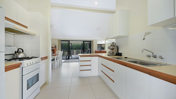 Una cocina moderna con muebles blancos, cocina a gas, hervidor y cafetera.